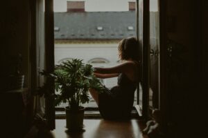 Woman sitting alone looking out window representing feeling hollow inside despite life looking fine